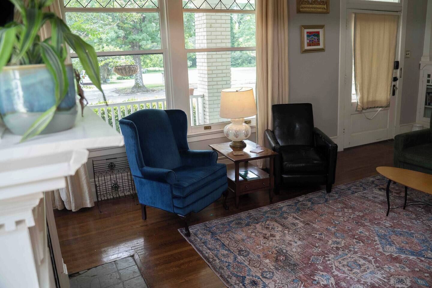 Une pièce comprenant un fauteuil bleu, une chaise en cuir noir, une table en bois avec une lampe et un tapis à motifs.