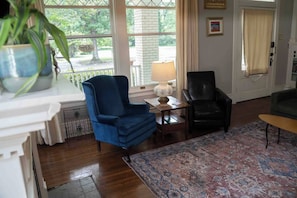 A room with a blue armchair, a black leather chair, a wooden table with a lamp, and a patterned rug. - Porch swing, 1920s home, walk to live music (Clarksdale)
