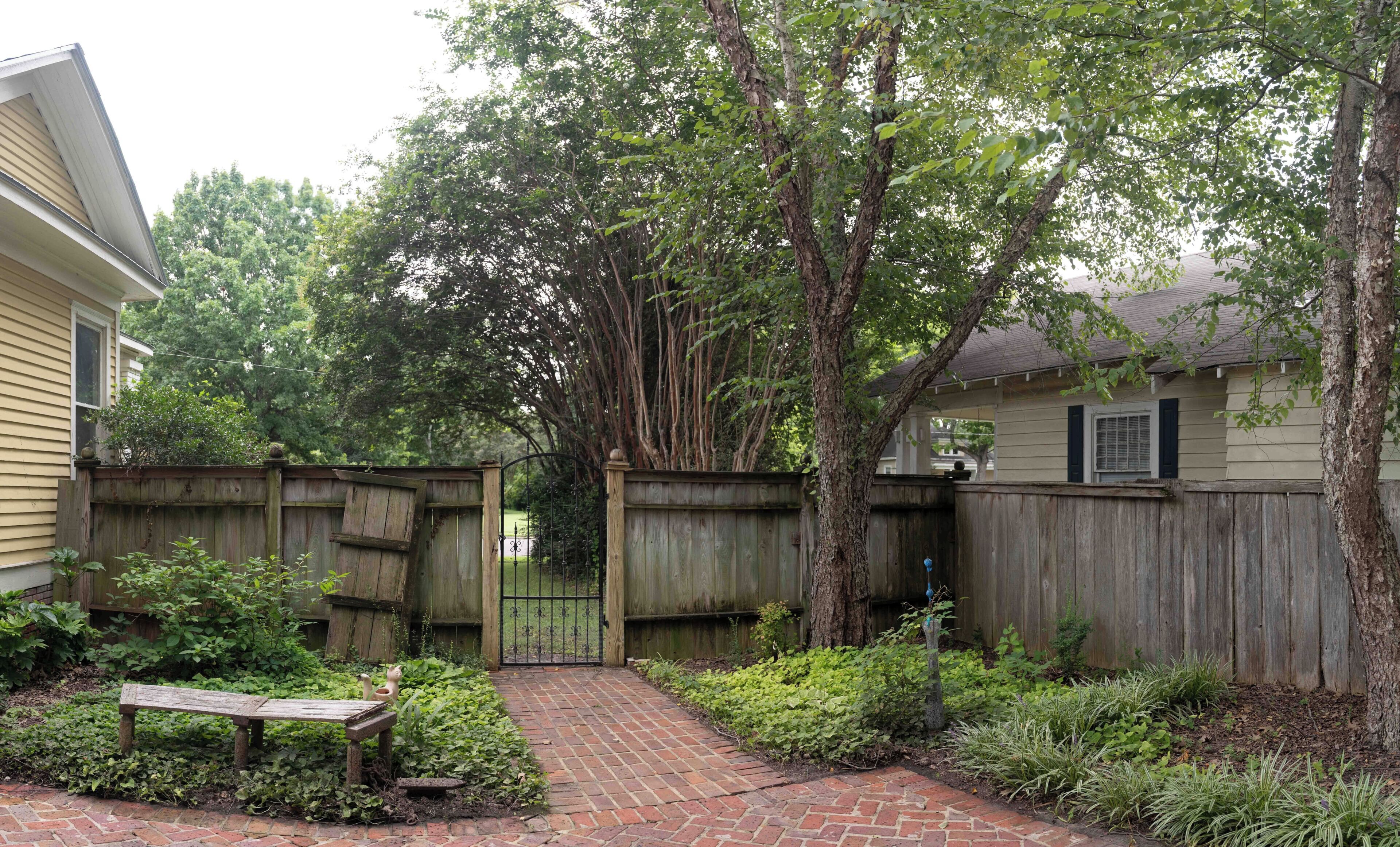 A backyard with a brick pathway, wooden fence, and a bench.