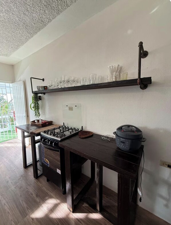 A kitchen with a gas stove, a built-in oven, a countertop with a rice cooker, and a shelf with glasses and utensils.