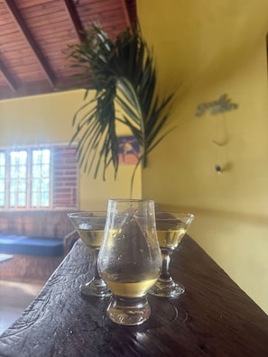 Ein Holztisch mit drei Gläsern einer klaren Flüssigkeit, möglicherweise Wasser, in einem Raum mit gelber Wand und einer Pflanze.