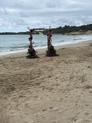 Een strand met een houten bogenpoort versierd met bloemen en begroeiing.