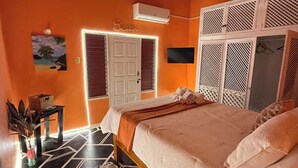 A bedroom with a bed, a nightstand, a wall-mounted TV, and a door leading to another room. -  4- bedroom/ 12 bed-Oracabessa Seaside Jamaican Manor  Private Beachfront Access (Oracabessa)