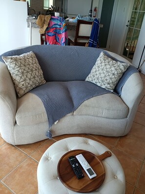 Ein Wohnzimmer mit einer Couch, zwei gemusterten Kissen, einer Fernbedienung und einem Holztablett.