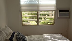 Ein Schlafzimmer mit einem Bett, Kissen, einem Fenster mit Jalousien und einer Klimaanlage.