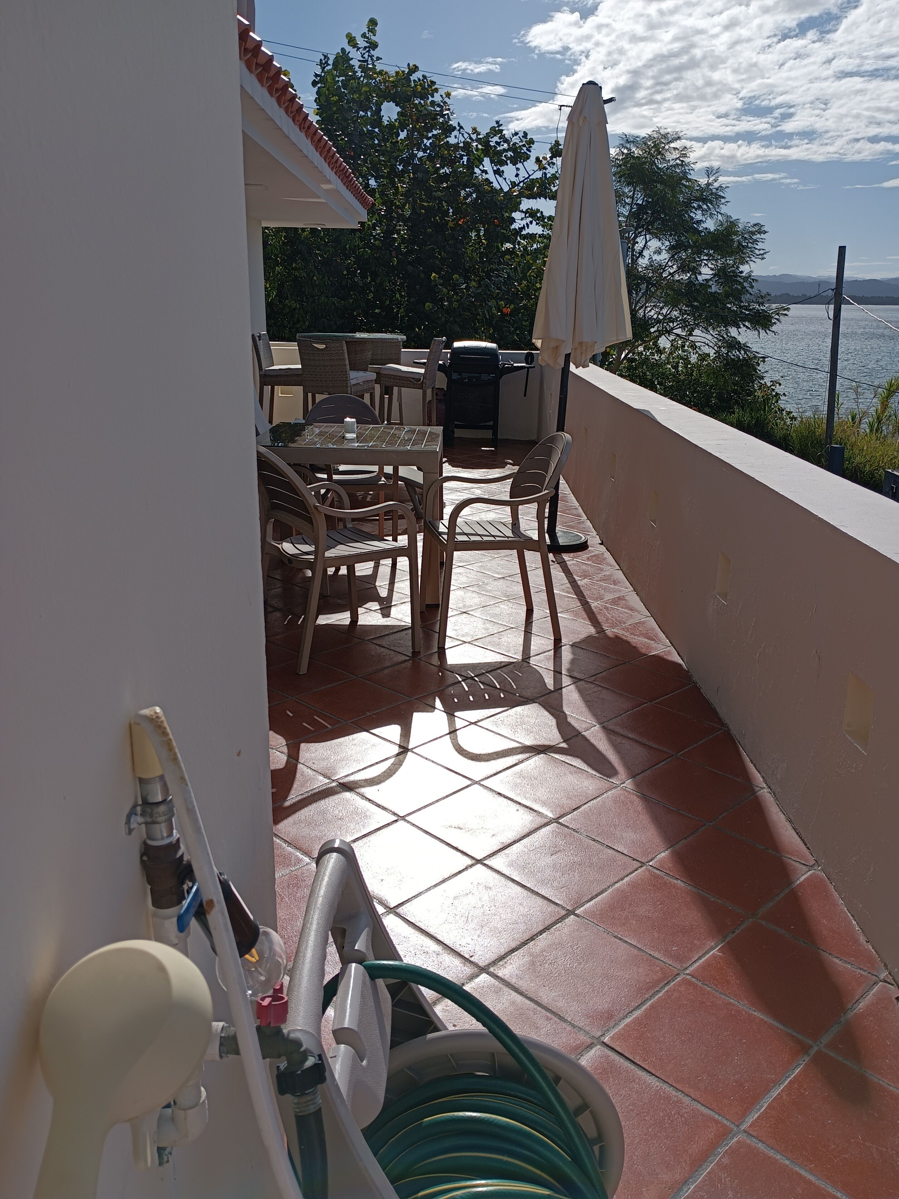 A balcony with outdoor furniture, a grill, and a hose.