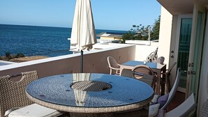 Ein Balkon mit rundem Tisch und Korbstühlen, mit Blick auf das Meer.