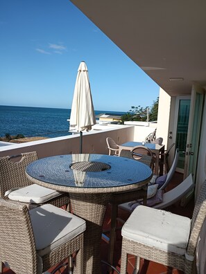 Ein Balkon mit rundem Tisch und Korbstühlen, mit Blick auf das Meer.