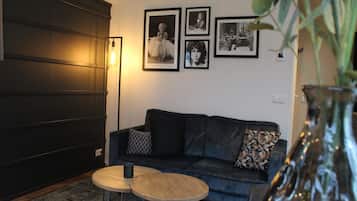 A living room with a dark-colored sofa, two round wooden tables, and a large vase with greenery.