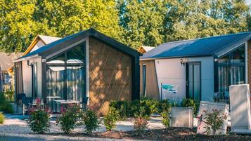 Un alojamiento tipo autocaravana moderno con un área de estar cubierta al aire libre, un pequeño jardín y un camino de entrada pavimentado.