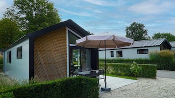 A modern building with a dining area featuring a table and chairs, an umbrella, and a gravel path.