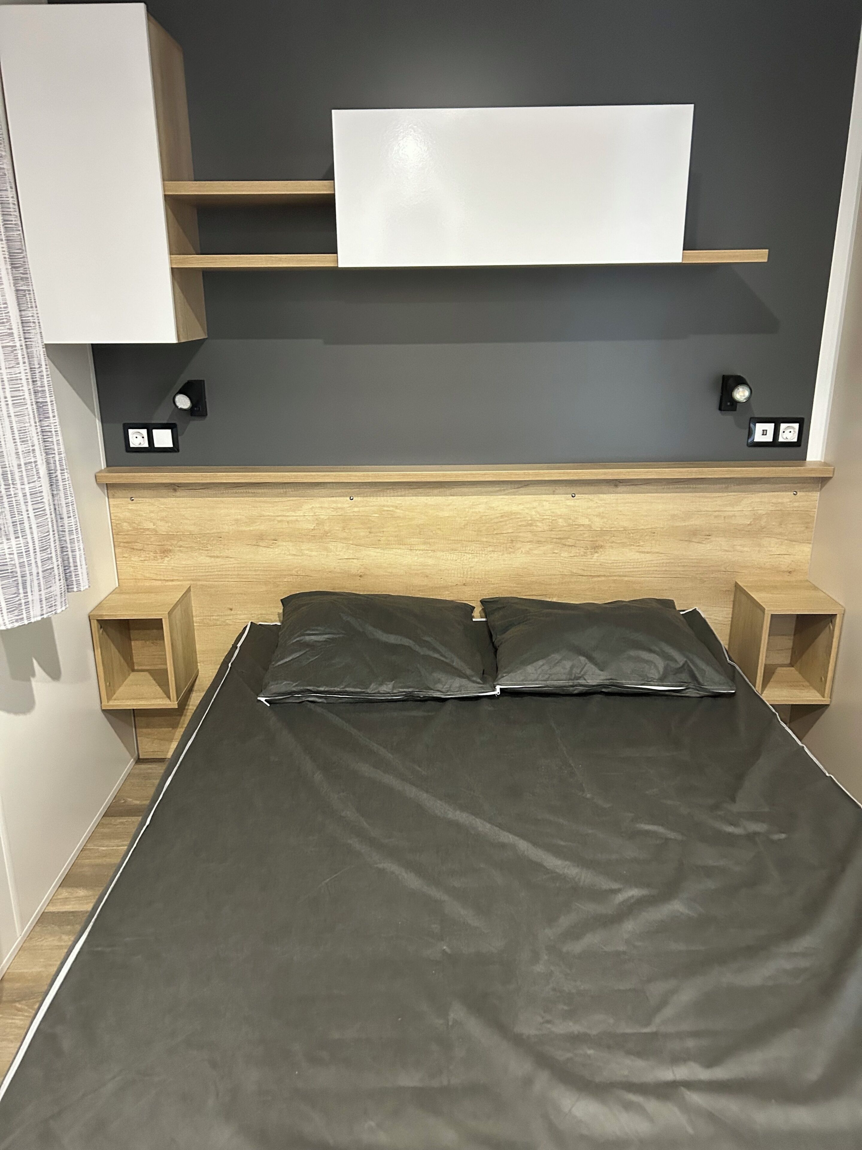 Un dormitorio con cama, cabecera de madera, mesitas de noche, repisa en la pared y televisor de pantalla plana.