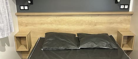 A bedroom with a bed, wooden headboard, bedside tables, a wall-mounted shelf, and a flat-screen TV.