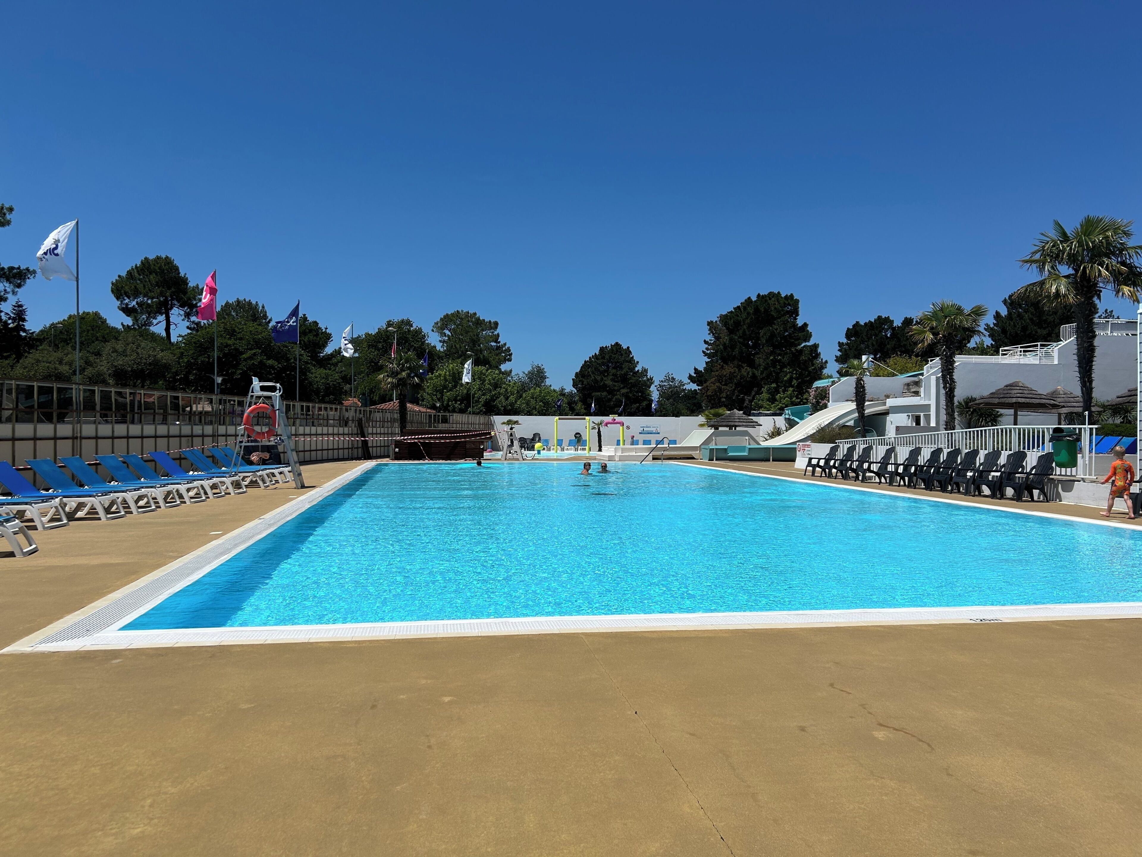 A swimming pool with blue water, surrounded by lounge chairs and a lifeguard stand.