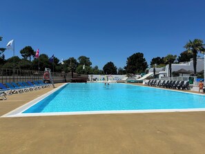 Ein Schwimmbecken mit blauem Wasser, umgeben von Liegestühlen und einem Rettungsschwimmerstand.