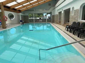 Una piscina interior amb vistes clares a l'exterior, un flotador i una filera de cadiretes al costat de la piscina.