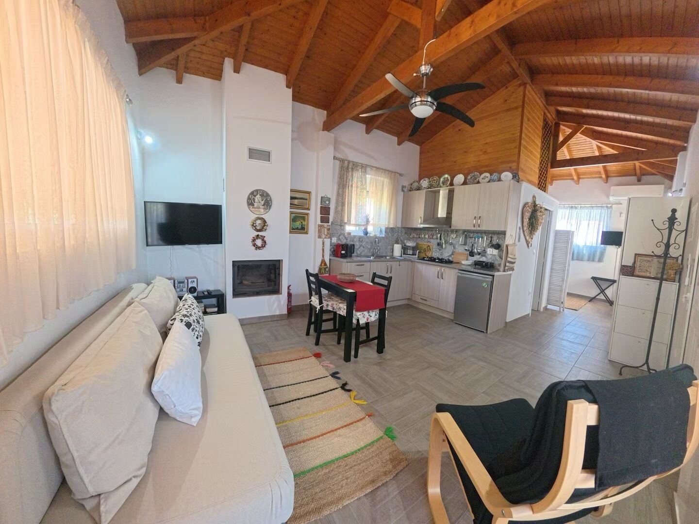 Una sala de estar con sofá, una mesa de comedor y sillas, una cocina con armarios y un refrigerador, y un ventilador de techo.