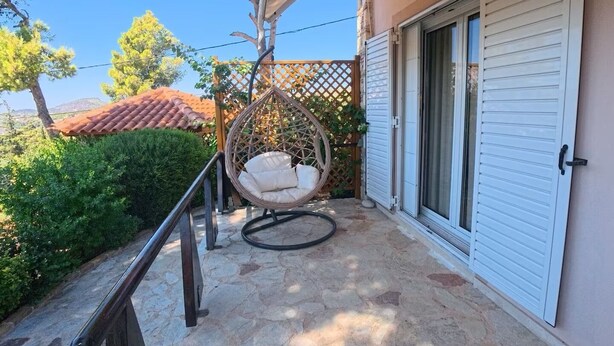 Un espace extérieur abrité, doté d’un sol en pierre, d’un fauteuil suspendu et d’une porte avec une fenêtre coulissante en verre.