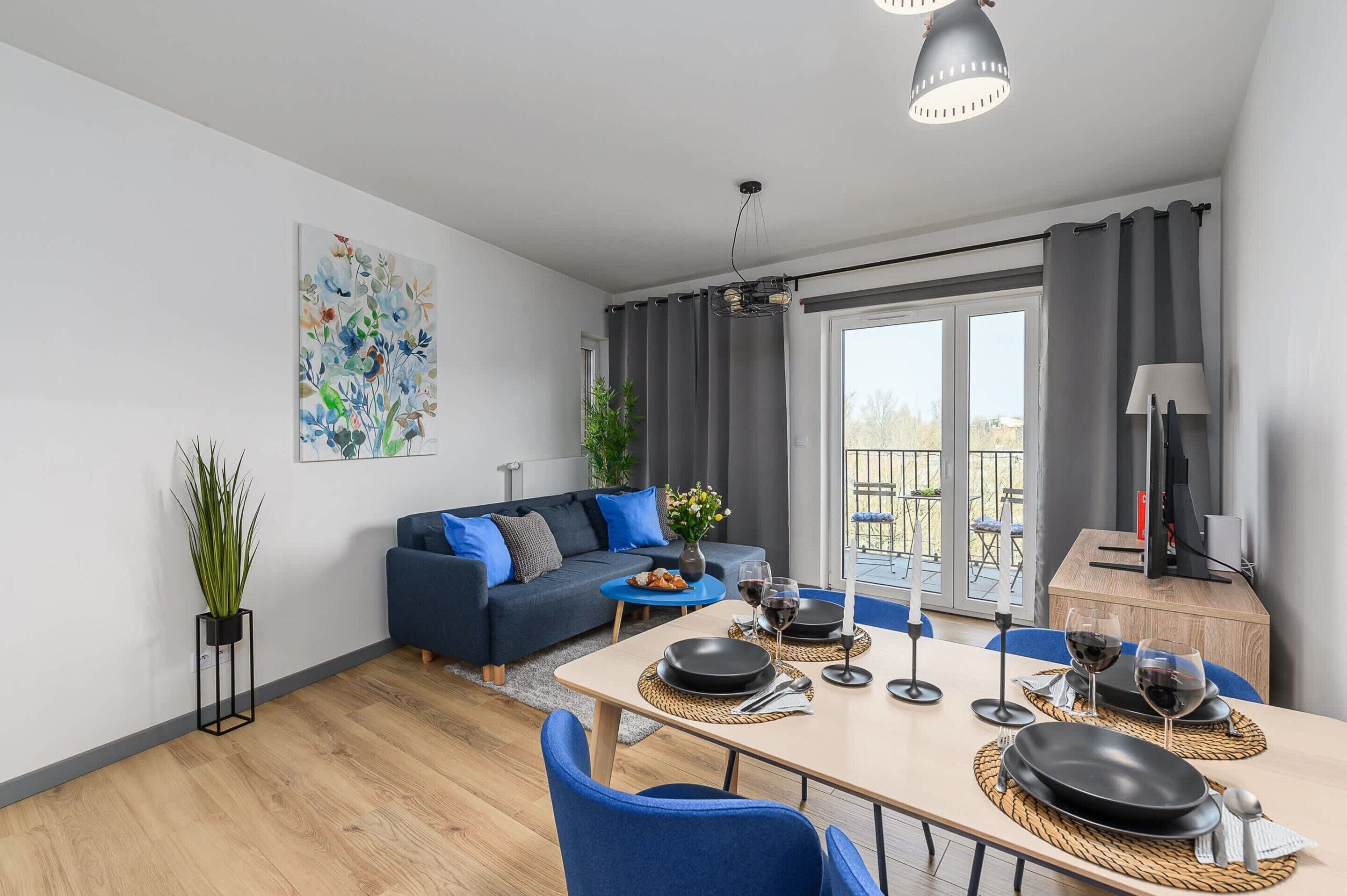 A modern living room with a sofa, dining table, and a balcony with curtains.