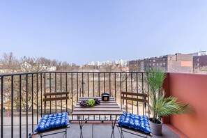 A balcony with a wooden table, two blue patterned cushions, a potted plant, and a bowl of grapes. - Flat Near Koneser Center (Warsaw)