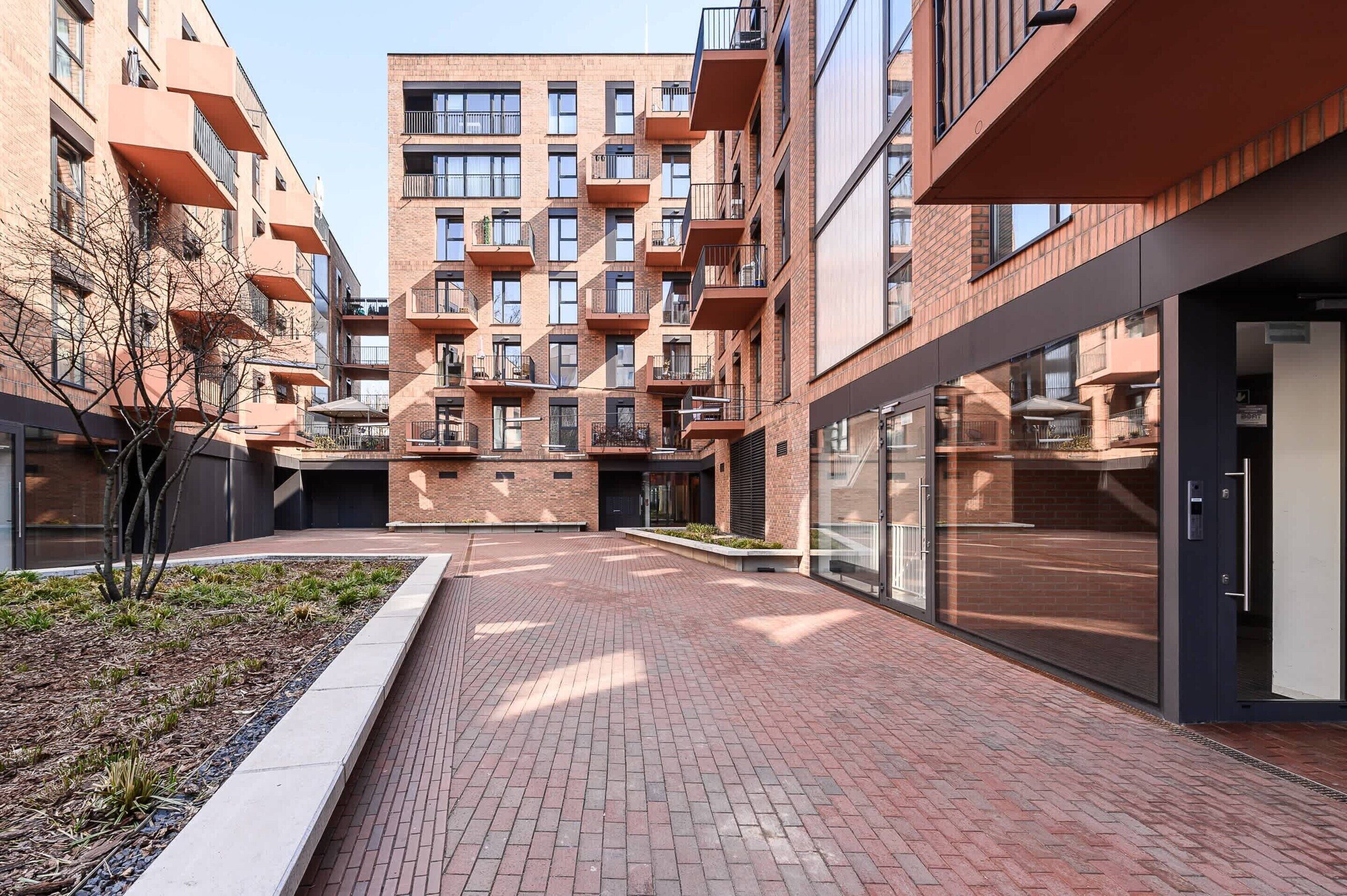 A modern apartment building with multiple balconies, a brick facade, and a paved courtyard.