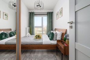A modern bedroom with a large bed, a bedside table, a nightstand, and a view of the outdoors. - Flat Near Koneser Center (Warsaw)