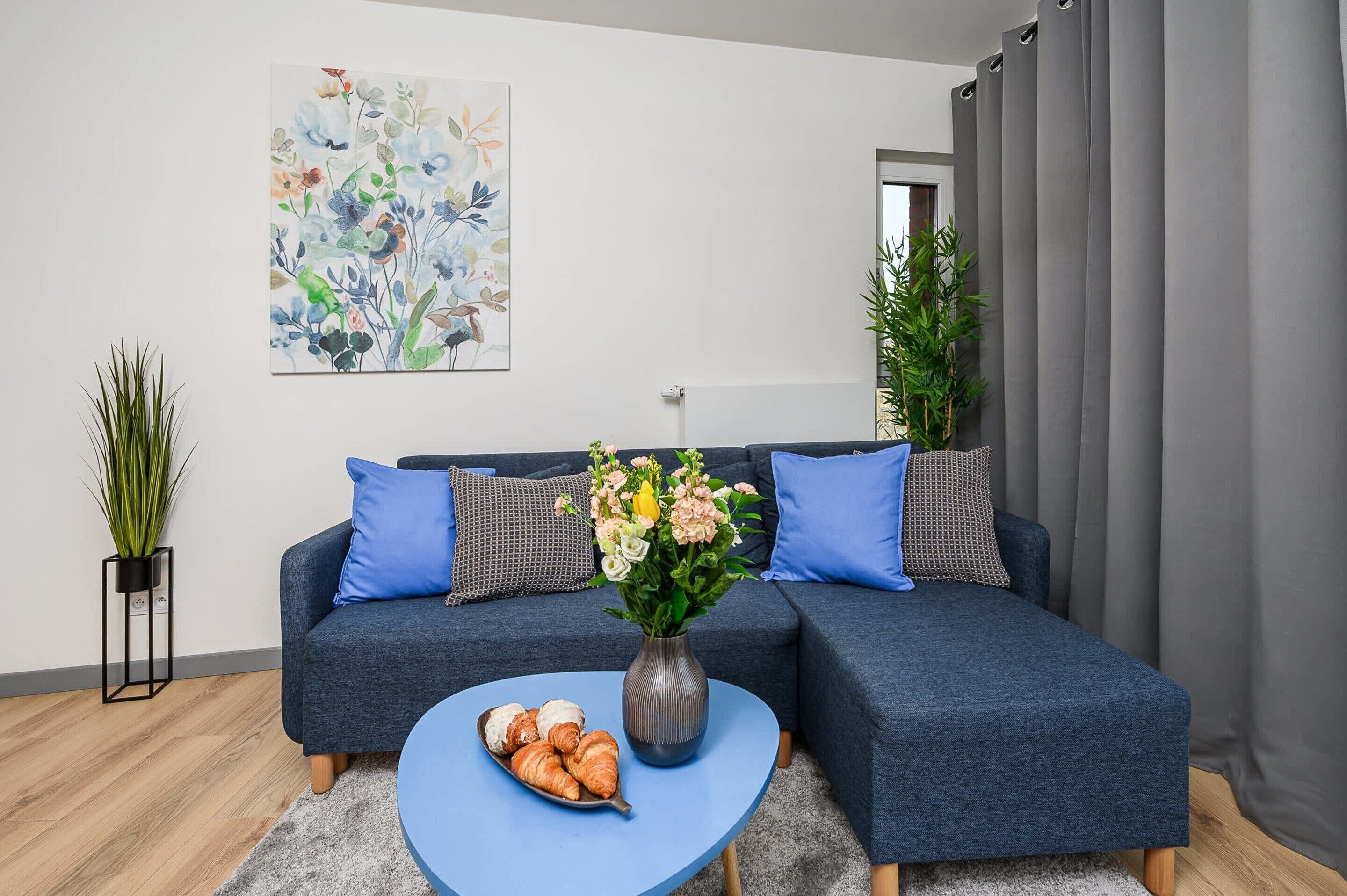 A modern living room with a blue sofa, a coffee table, and a floral arrangement.