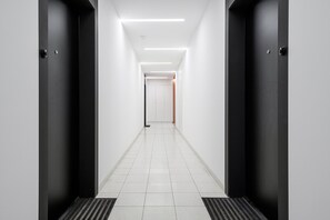 A corridor with two black doors on either side, white walls, and a tiled floor. - Flat Near Koneser Center (Warsaw)