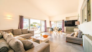 A living room with a sofa, a coffee table, and a TV. There is a dining area with chairs and a table. - Sophisticated villa with heatable pool (Albufeira)