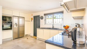 A modern kitchen with stainless steel appliances, a sink, and a window with decorative bars. - Sophisticated villa with heatable pool (Albufeira)