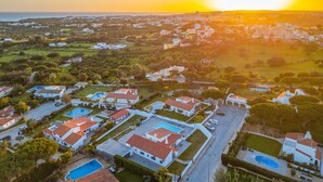 An aerial view of a residential area with houses, swimming pools, and a clear view of the sunset over the ocean. - Sophisticated villa with heatable pool (Albufeira)