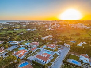 An aerial view of a residential area with houses, swimming pools, and a clear view of the sunset over the ocean. - Sophisticated villa with heatable pool (Albufeira)