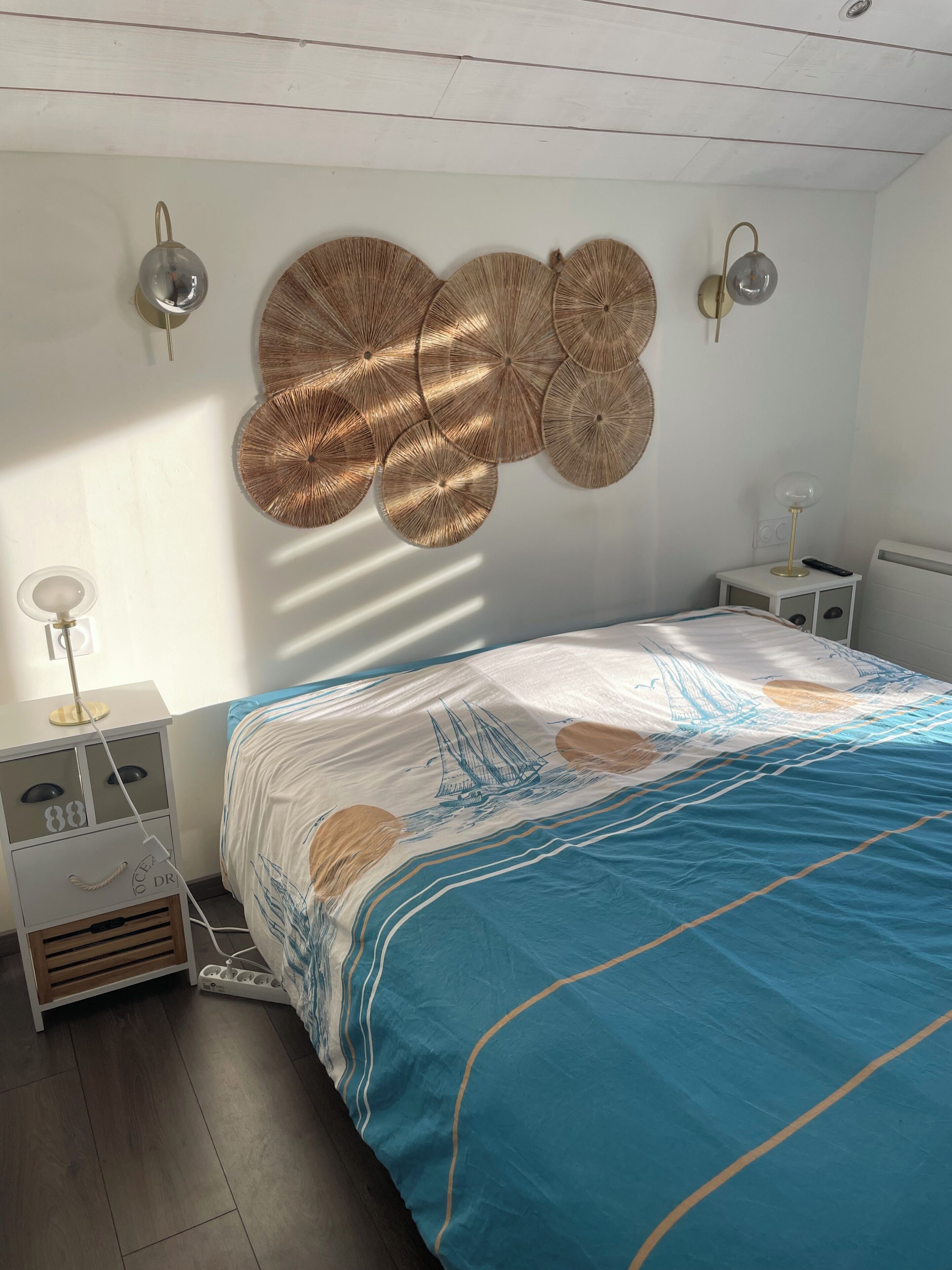 A bedroom with a bed, bedside tables, wall sconces, and a decorative wall hanging.