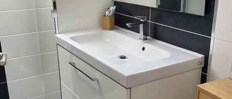 Un baño con lavamanos blanco, espejo y mueble de madera.