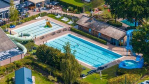 Ein großer Außenpool mit Rutsche und Wasserspielbereich, umgeben von Liegestühlen und einem kleinen Gebäude.