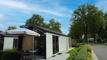 A modern outdoor seating area with a table and chairs under a canopy, adjacent to a building with glass doors.