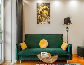 Ein grünes Sofa mit gelben und beigen Kissen, ein Couchtisch mit einer Zeitschrift und eine Stehlampe mit schwarzem Lampenschirm.