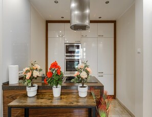 Une cuisine moderne avec des armoires blanches, une hotte de cuisinière en acier inoxydable et trois plantes en pot sur le comptoir.