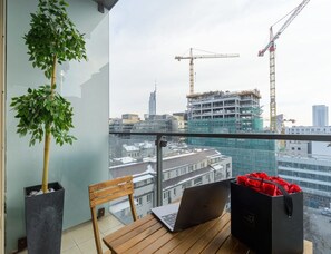 Un balcon avec un ordinateur portable, une chaise, un pot de fleurs et un sac contenant des objets rouges.