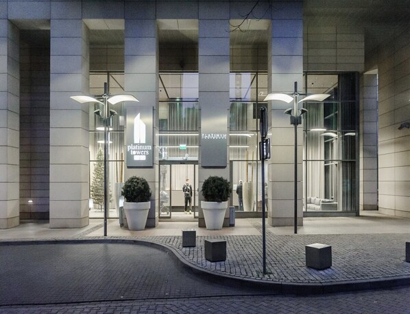 Un bâtiment moderne avec une entrée en verre, de grands pots de plantes et une enseigne indiquant « Platinum Towers ».
