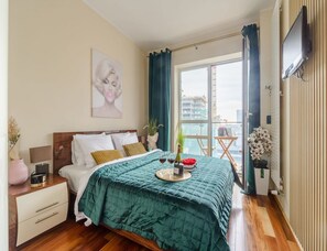 Une chambre à coucher avec un lit, une table de chevet, des rideaux, une fenêtre et un téléviseur.
