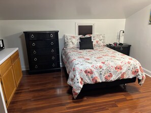 Un dormitorio con cama, cómoda, mesita de noche y lámpara de pared.