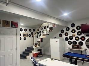 A room with a pool table, a refrigerator, a staircase, and walls decorated with vinyl records.