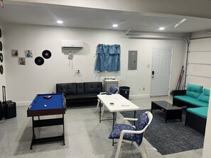 A room with a pool table, a sofa, a chair, a small table, and a door.