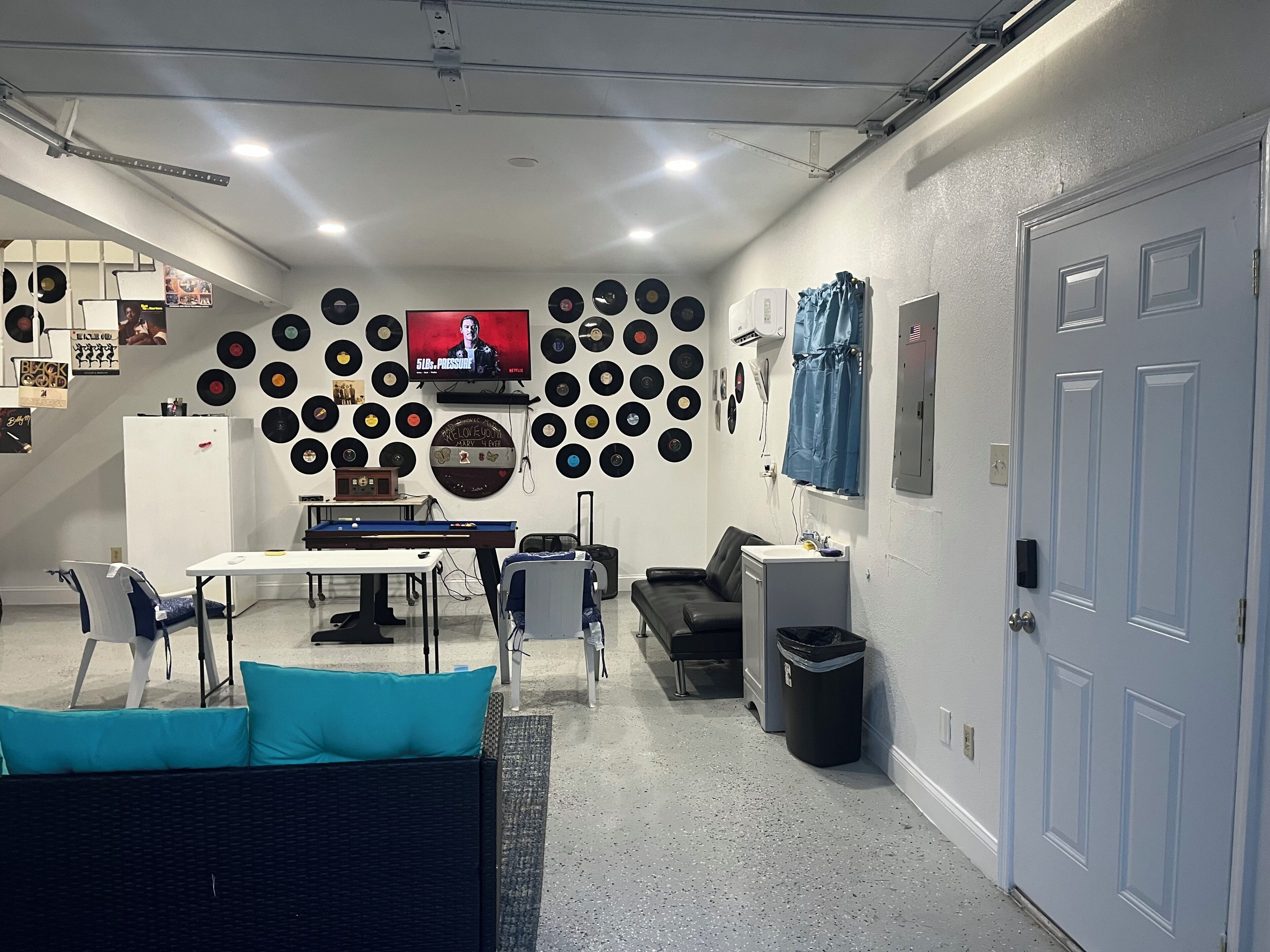 Una habitación con una pared llena de discos de vinilo, un televisor, una mesa de billar y una zona de estar.