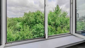 A window with a view of dense green foliage and a cloudy sky. - Sunlit Home With City Views (Warsaw)