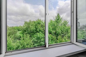 Ein Fenster mit Blick auf dichtes Grün und einen bewölkten Himmel.