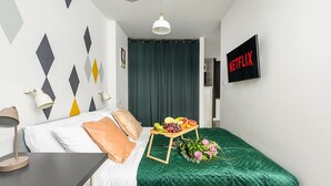 A hotel room with a bed, a small table with fruit and flowers, a wall-mounted TV, and a geometric wall design. - Sunlit Home With City Views (Warsaw)