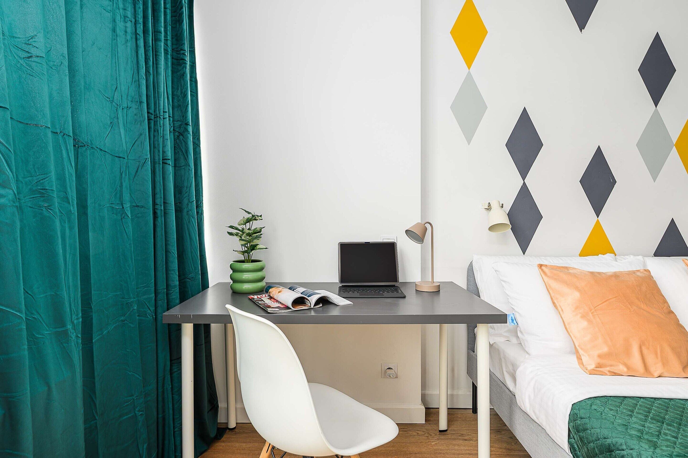Une chambre moderne équipée d’un bureau, d’un ordinateur portable, d’une chaise et d’un lit avec des oreillers.
