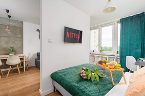 A modern bedroom with a green bedspread, a Netflix sign, a desk with a chair, and a window with curtains. - Sunlit Home With City Views (Warsaw)